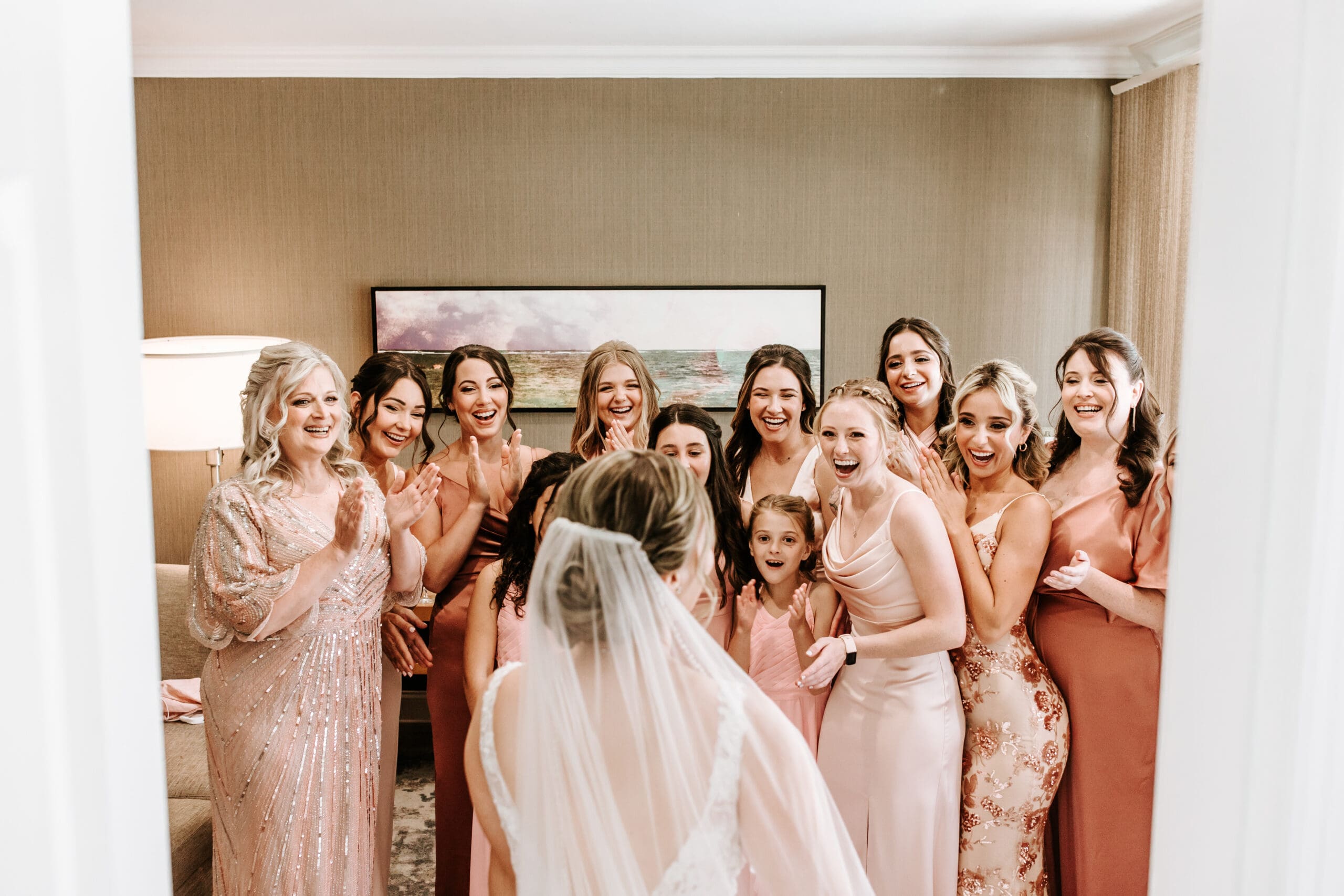 Group of bridesmaids in an array of blush dresses are shocked and brought to tears by the vision of the bride on her wedding day.