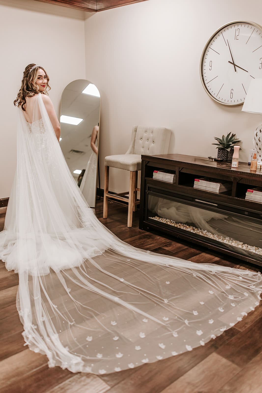 Running Deer Golf Club Getting Ready Space Stunning bride in Running Deer Golf Club Wedding getting ready space, with her cape draped over her shoulder on top of her train, looking back at the camera with a soft serious look.