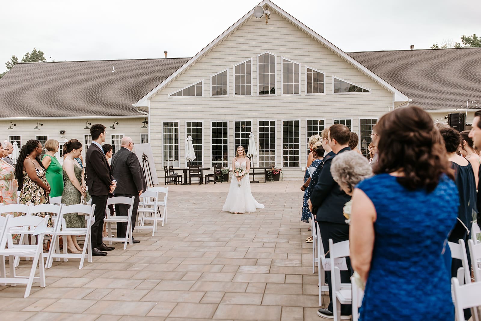 Stunning bride walking herself down the aisle , with ivory cape draped behind shoulder during a Summer Wedding Ceremony at Running Deer Golf Club