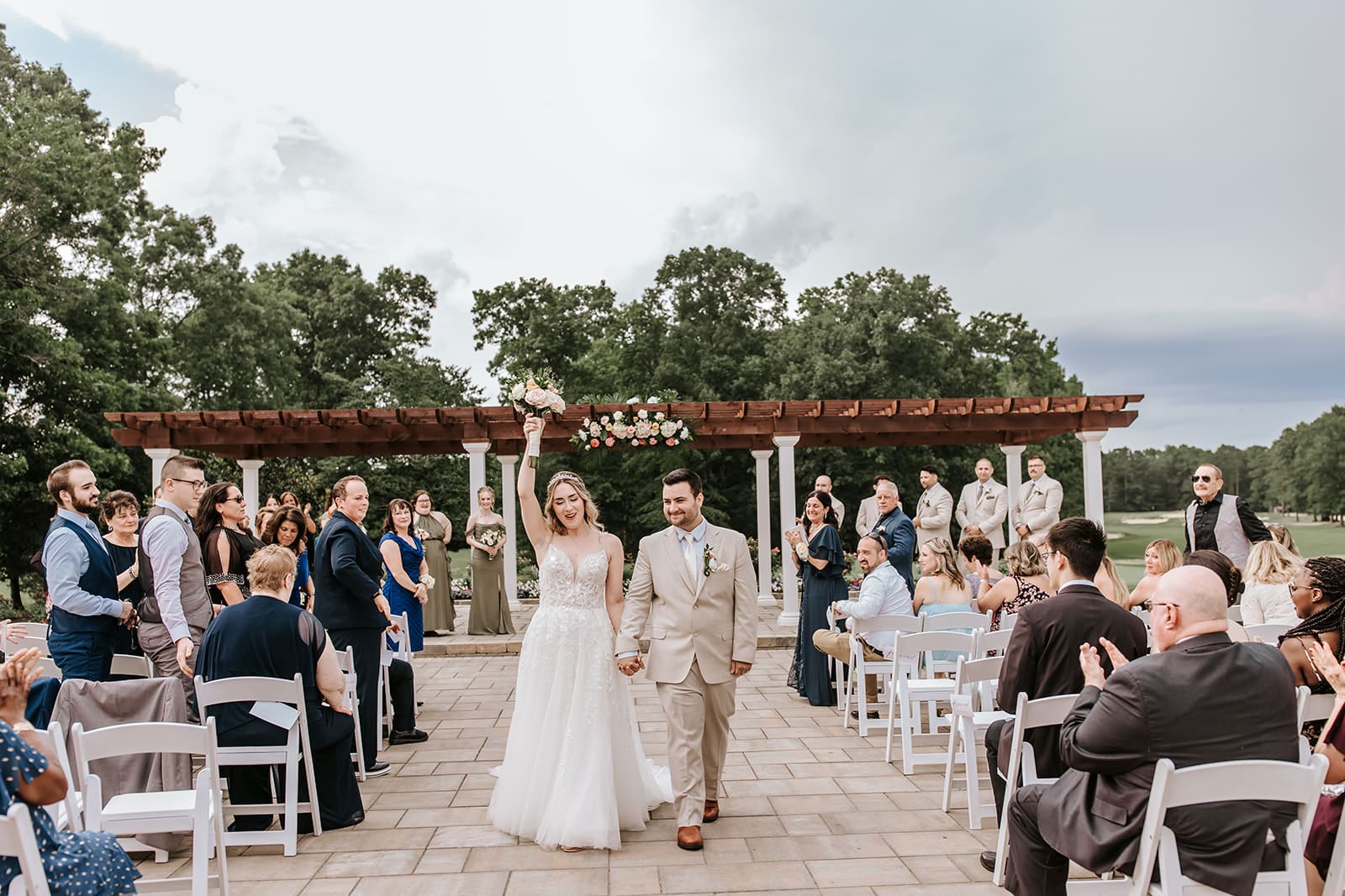 Bride excitedly holding up flowers, holding groom's hand while walking down the aisle, after their first kiss as husband a wife.