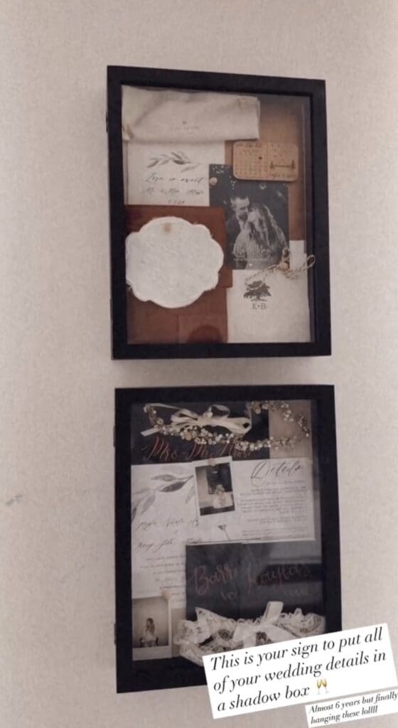 One Year Anniversary Gifts Photo of two black, glass shadow boxes with wedding flat-lay details, hung on white wall. The boxes are filled with heirloom items, such as handwritten wedding envelope, bride's golden hair piece, lace, vow books and garter.