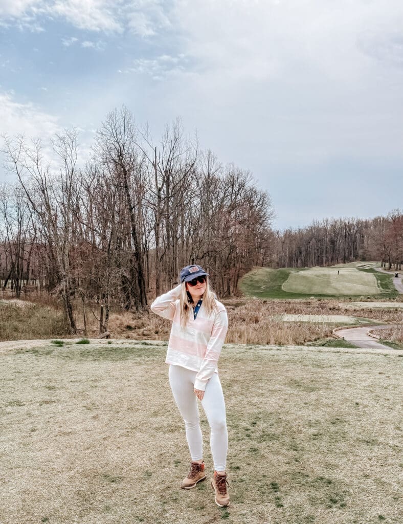 Woman dressed in casual activewear and sunglasses poses on a golf course at The Preserve at Eisenhower Golf Course in Annapolis, Maryland, with early spring trees and fairways in the background.