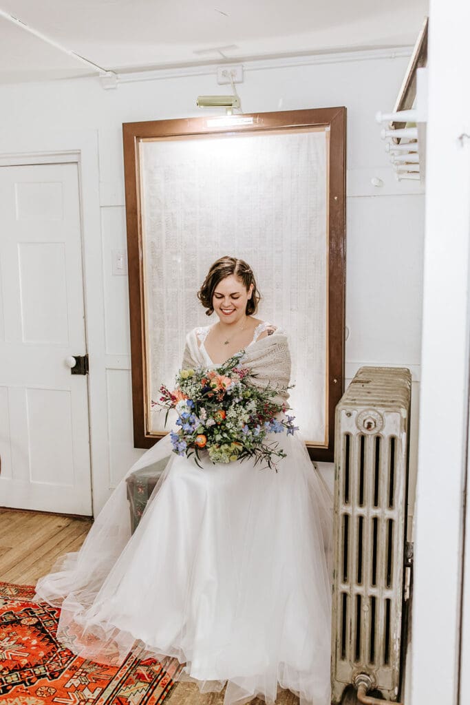 Bride sitting inside London Grove Quaker Meeting House in Kennett Square, PA, holding a colorful spring bouquet before her intimate Chester County wedding ceremony.