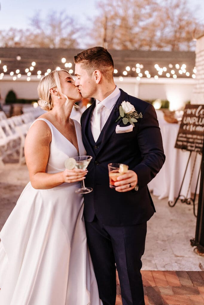 Bride and groom toast with cocktails under string lights during their fall wedding reception at The Grove at Centerton.