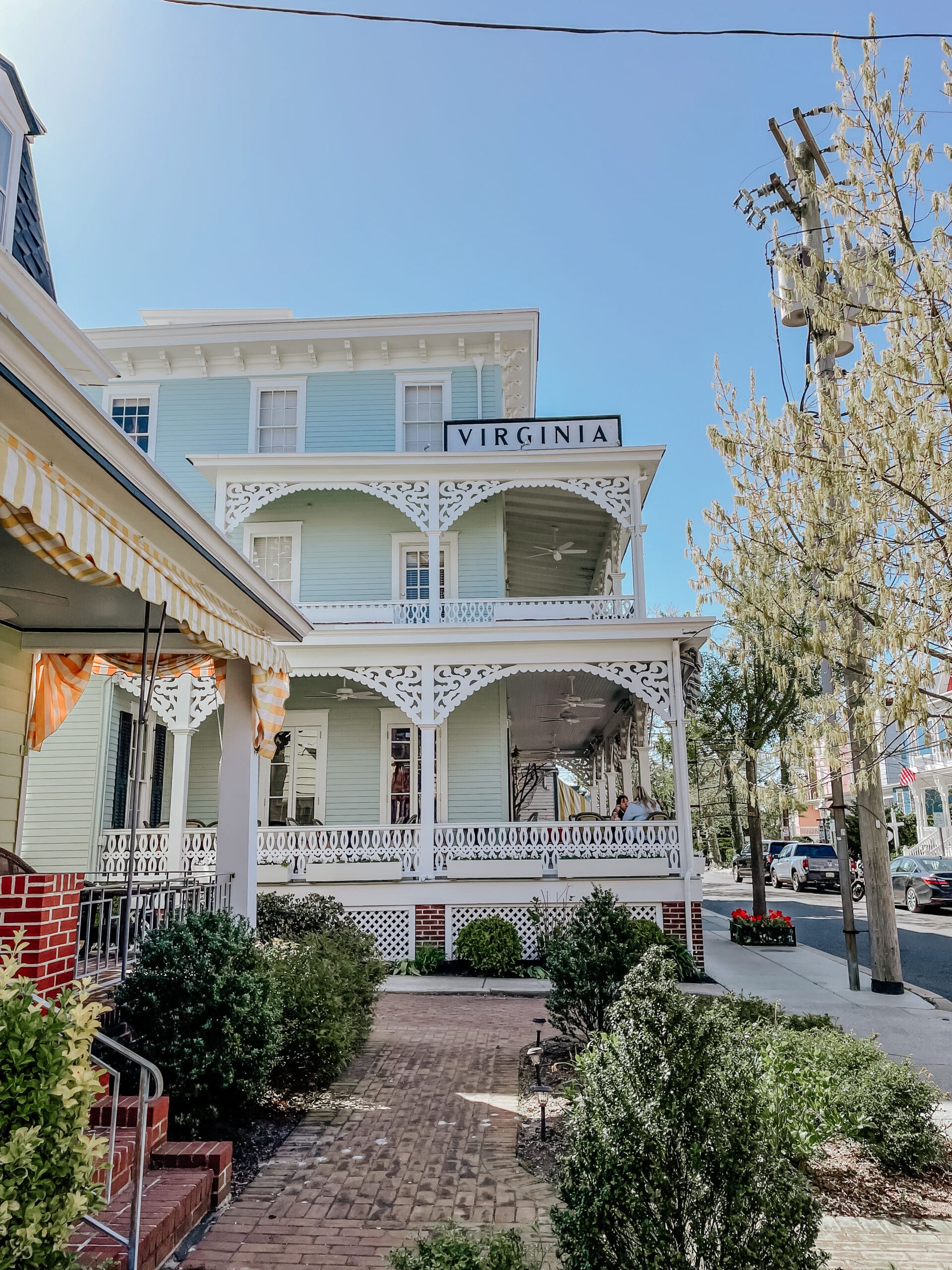 Exterior view of The Virginia Hotel in Cape May, NJ—a beautifully restored Victorian-style inn with pastel blue siding, white ornate trim, and a charming wraparound porch.
