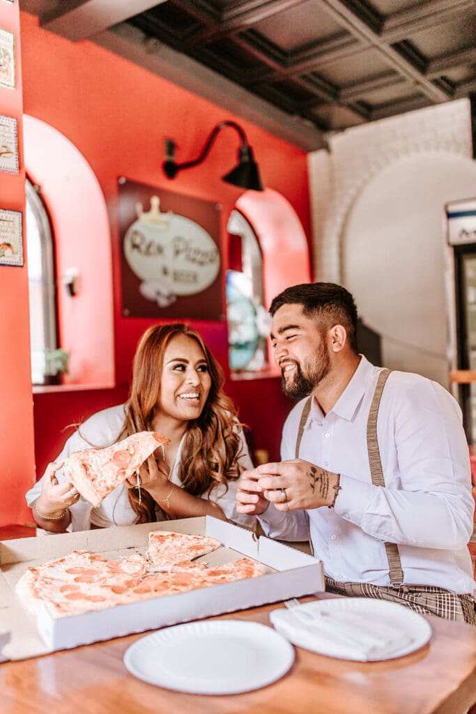 Couple sharing a pizza at Rex Pizza & Beer during a playful, casual engagement session in Center City Philadelphia, smiling and enjoying their time together indoors.