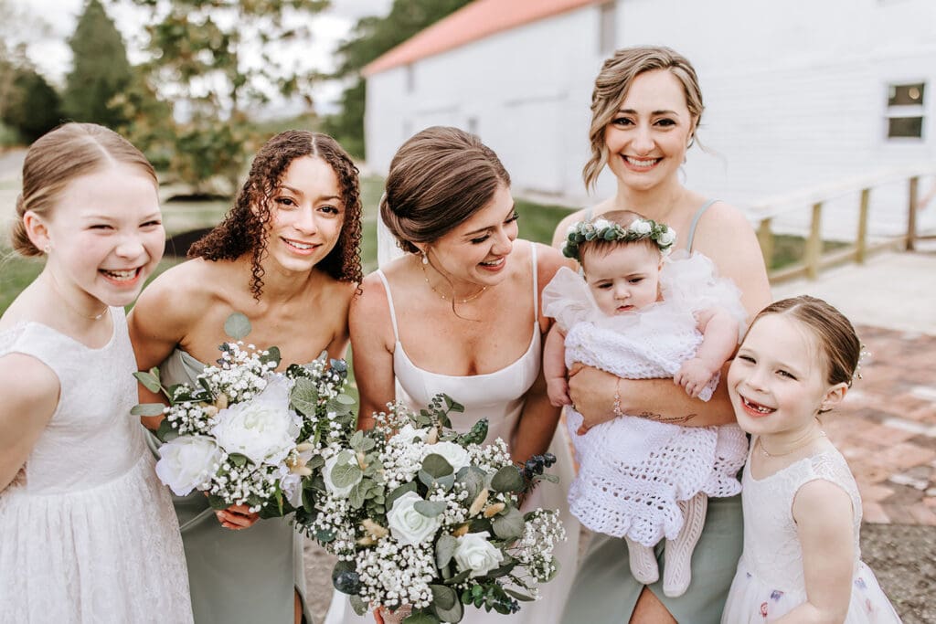Bride laughing with her bridesmaids and flower girls outside the historic white barn at Eagle Manor in Bridgeton, New Jersey.