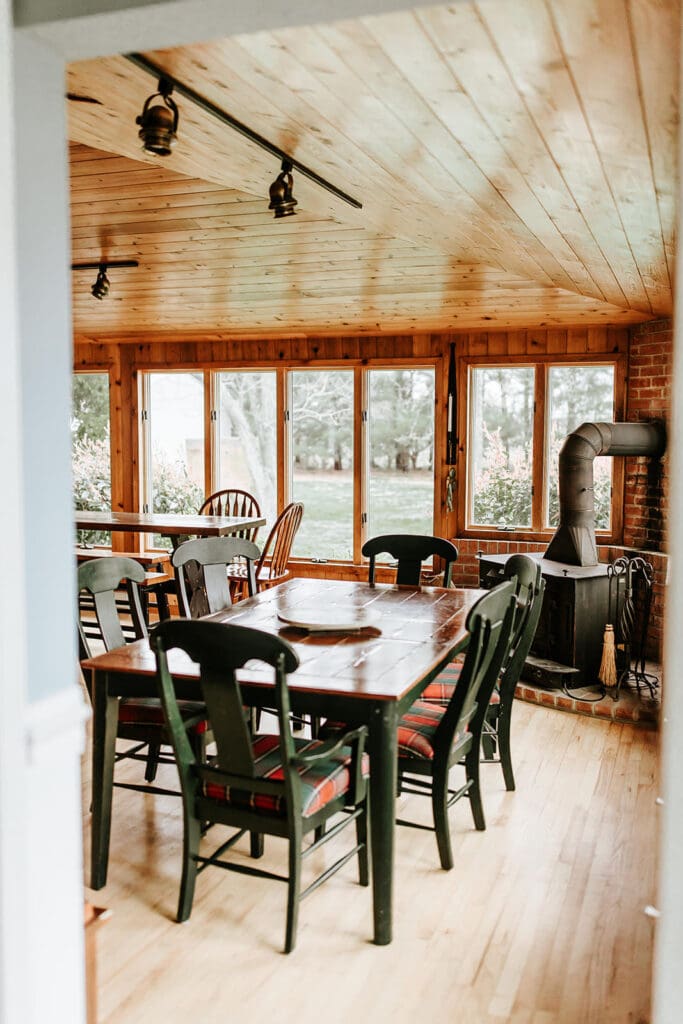 Cozy dining room at the historic Manor House at Eagle Manor in Bridgeton, New Jersey, featuring wood-paneled ceilings, large windows, and a rustic stove.