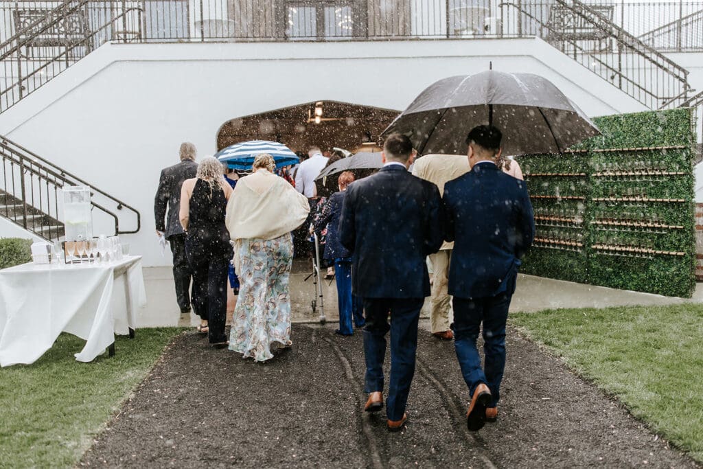 Wedding guests walking through heavy rain with umbrellas as they head inside the café for a makeshift ceremony at Renault Winery in Egg Harbor City, NJ.