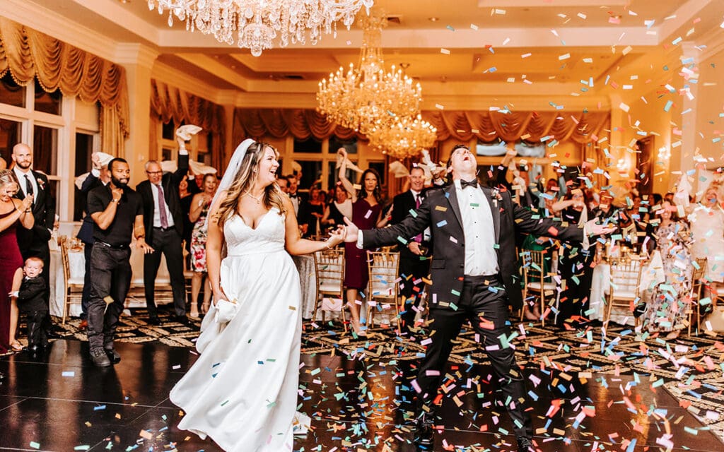 Bride and groom celebrating with colorful confetti on the dance floor under crystal chandeliers at a vibrant Philadelphia wedding.