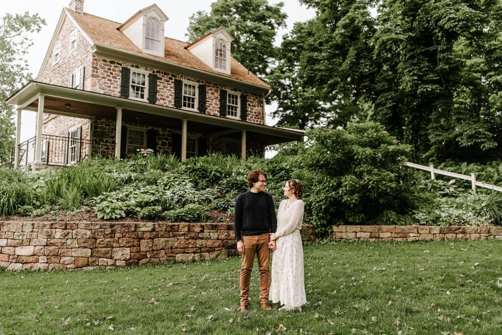 Engaged couple laughing and embracing in front of the iconic red covered bridge at Historic Poole Forge in Chester County, Pennsylvania during their spring engagement session.