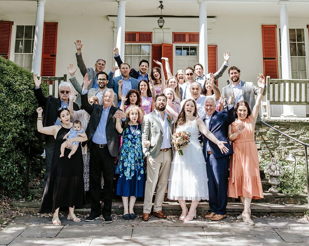Bride and groom celebrating with 24 family members during an intimate Highlands Mansion wedding in Philadelphia, group photo outside the historic venue.