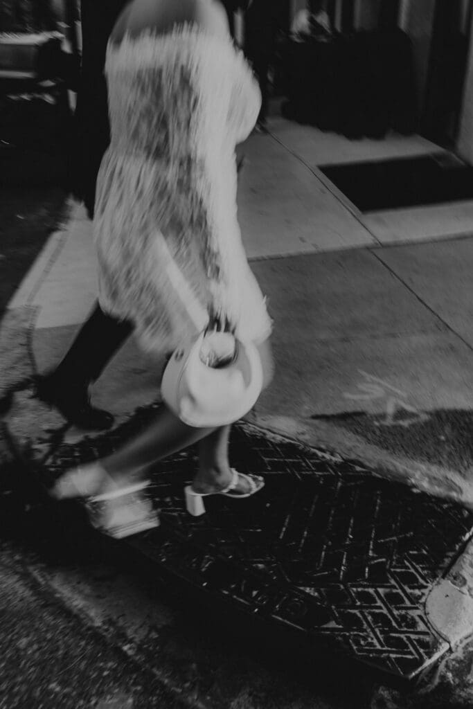 Artistic black and white photo of bride walking during Philadelphia engagement session in Old City, candid motion shot with lace dress and handbag.