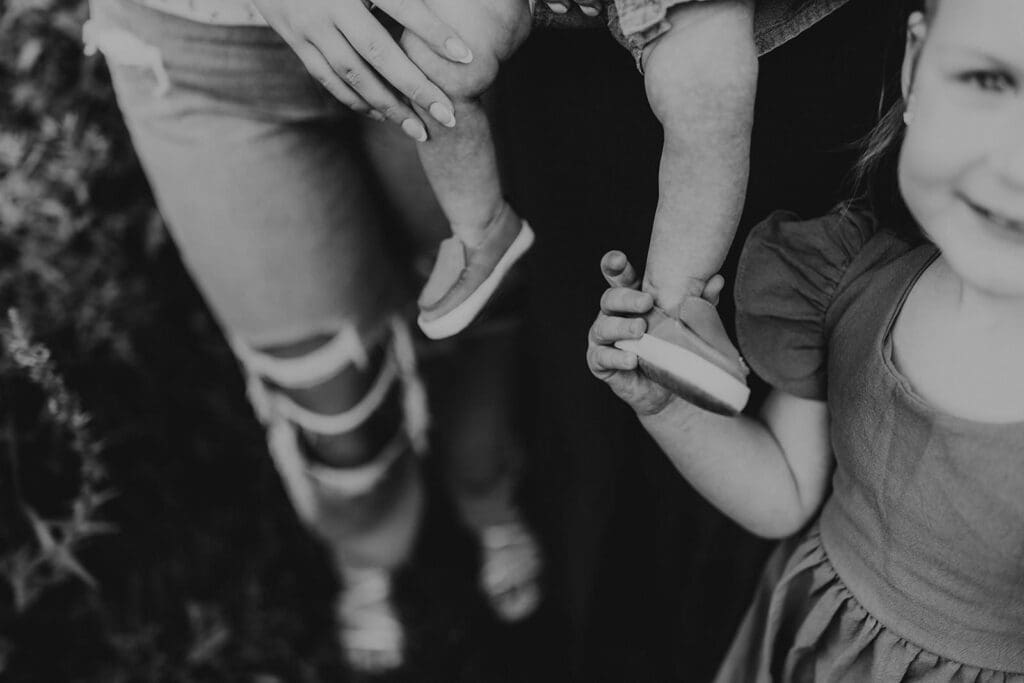 Close-up black and white photo of a little girl holding her baby brother’s foot during a family photography session in Chester County.