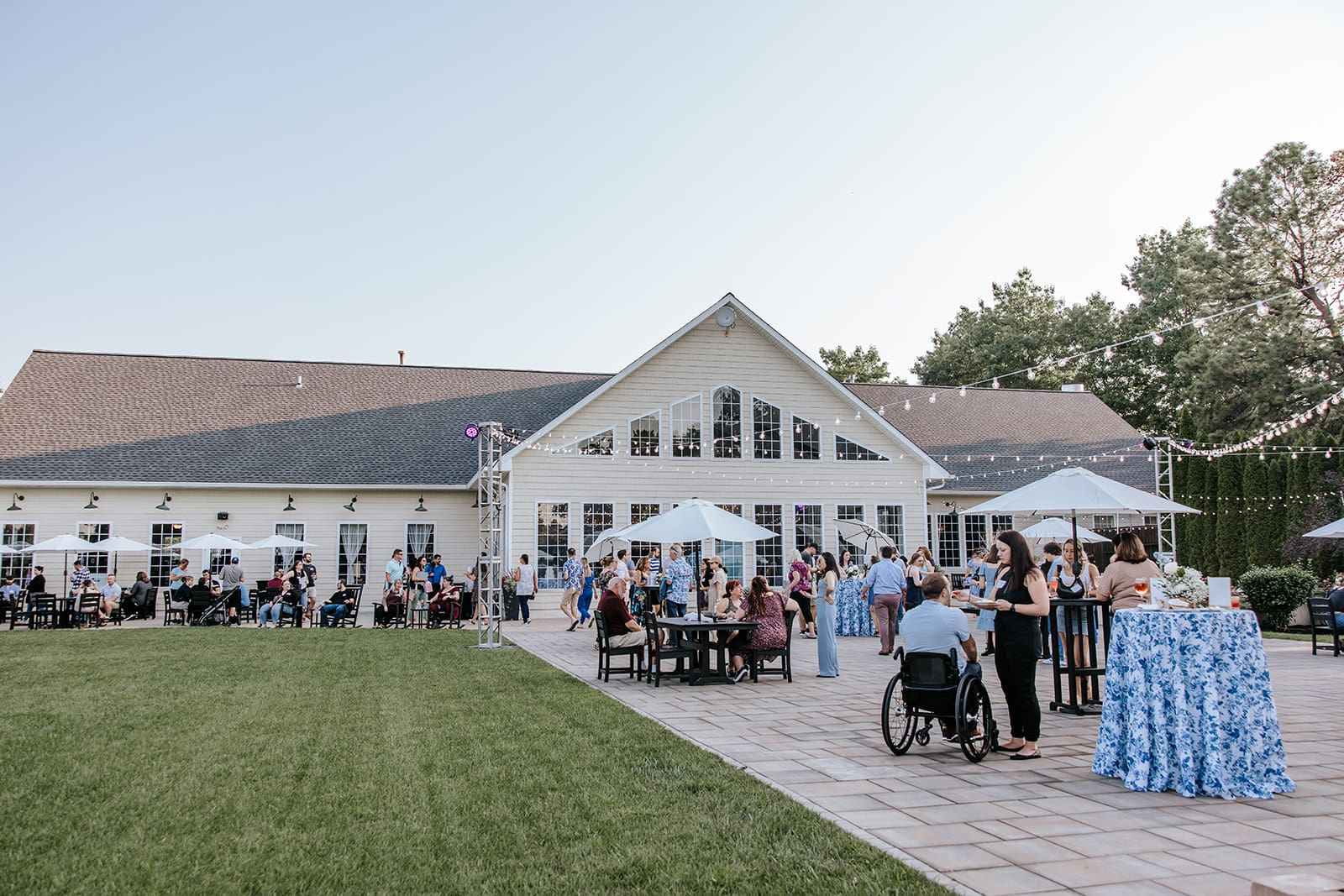 Cocktail hour wedding guests standing outside of the ballroom windows at Running Deer Golf Club during spring, surrounded by blooming trees and natural greenery, with blue floral table cloths.