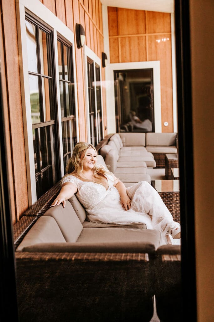 Bride relaxing and smiling on outdoor lounge seating along the wrap-around porch at Camden County Boathouse.
