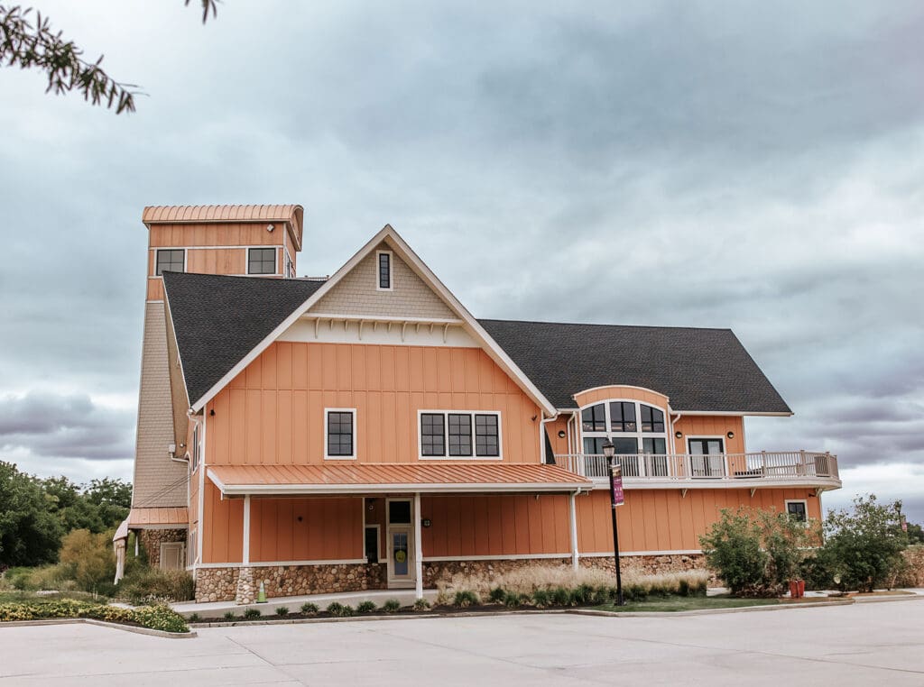 Camden County Boathouse wedding venue exterior with orange siding, stone foundation, and observation tower under a cloudy sky.