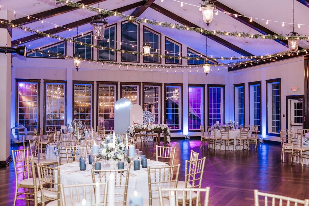 Elegant wedding reception inside the Grand Ballroom at Running Deer Golf Club, featuring string lights, gold chiavari chairs, and large windows creating a romantic atmosphere.