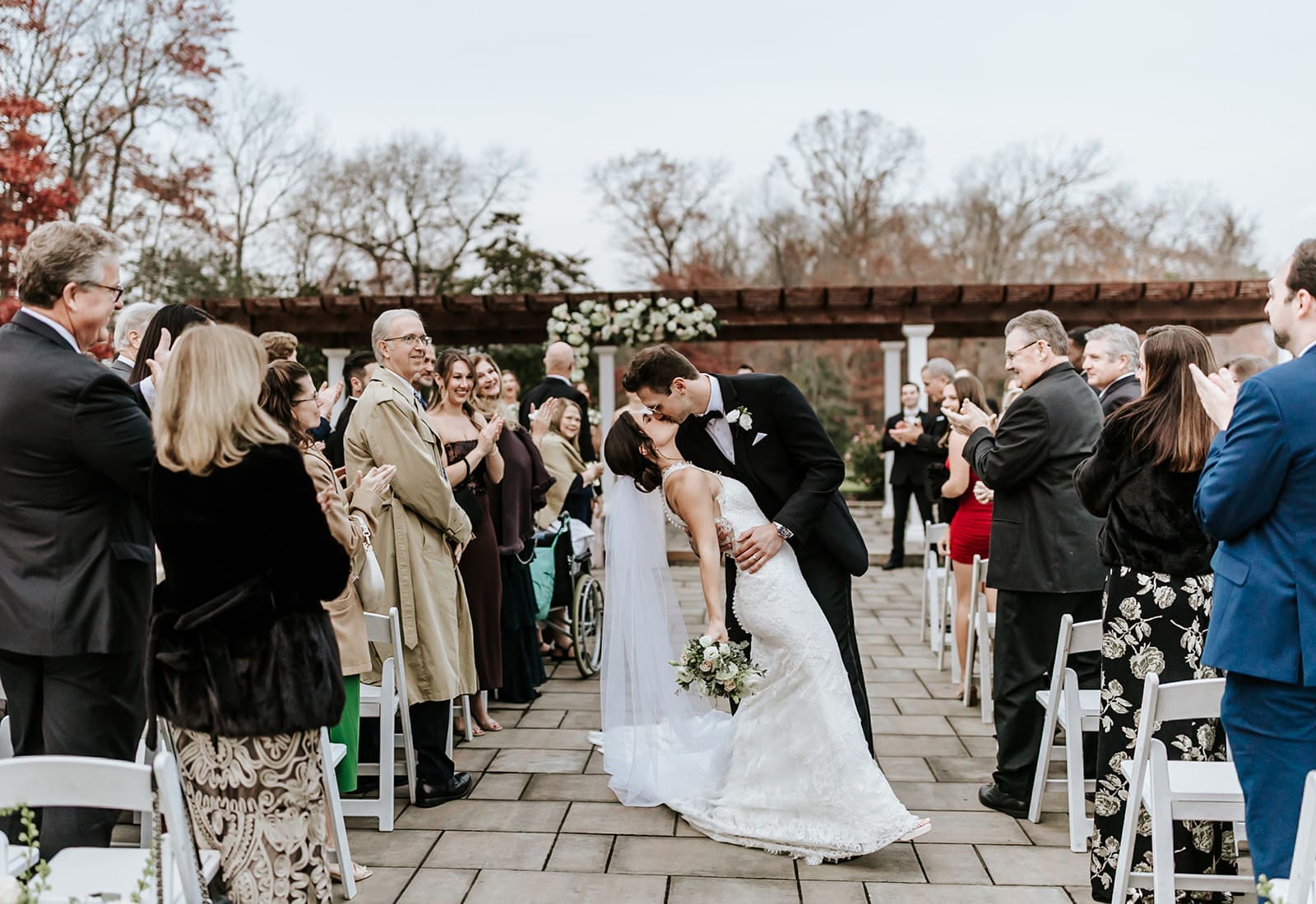 Bride and groom sharing a dip kiss down the ceremony aisle at Running Deer Golf Club while guests applaud in Pittsgrove, NJ.