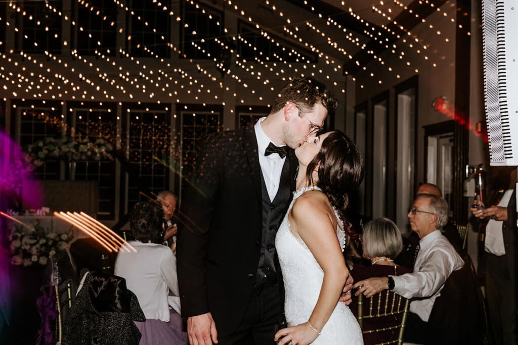 Bride and groom sharing a kiss under twinkle lights during their reception at Running Deer Golf Club in Pittsgrove, NJ.