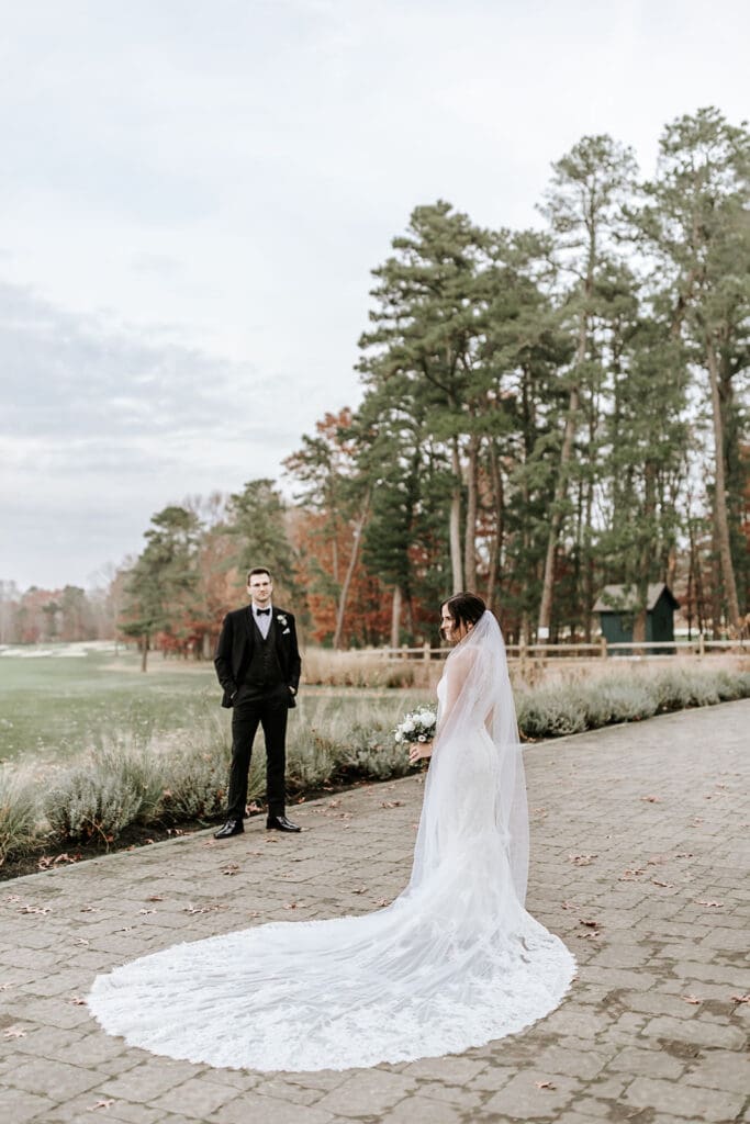 Bride walking toward groom for their first look on the tree-lined path at Running Deer Golf Club in Pittsgrove, NJ.
