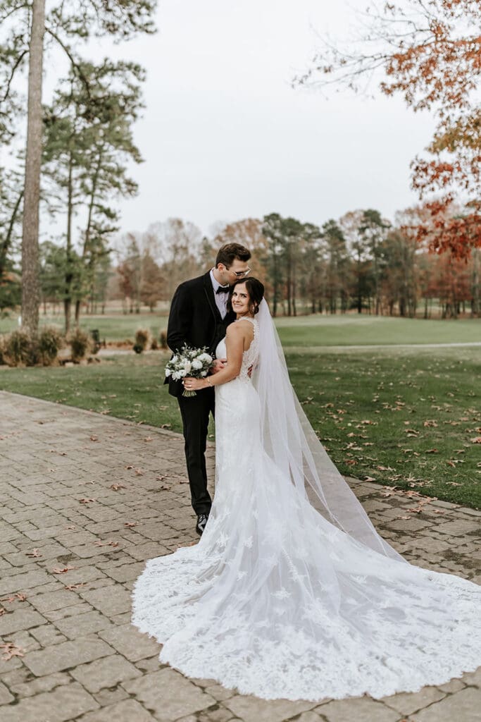 Bride and groom standing together on the stone path at Running Deer Golf Club with fall trees in the background.