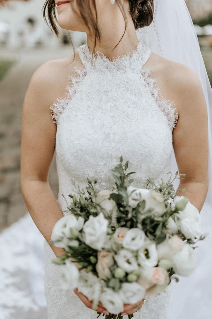 Close-up of the bride’s lace halter wedding dress and white floral bouquet at Running Deer Golf Club.