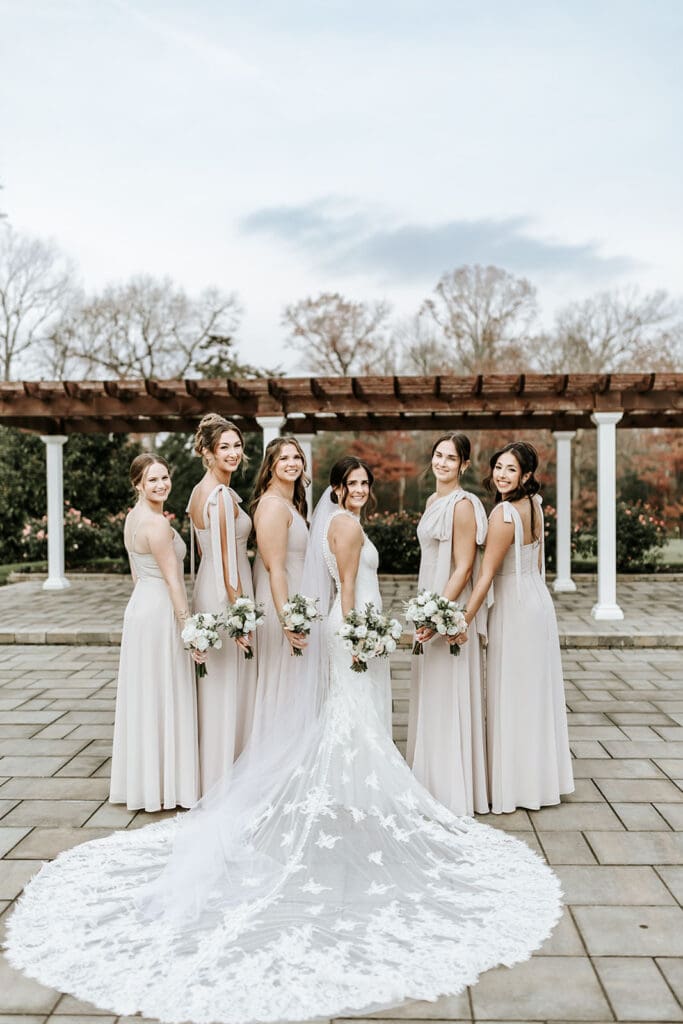 Bridesmaids holding white bouquets and standing behind the bride under the pergola at Running Deer Golf Club.