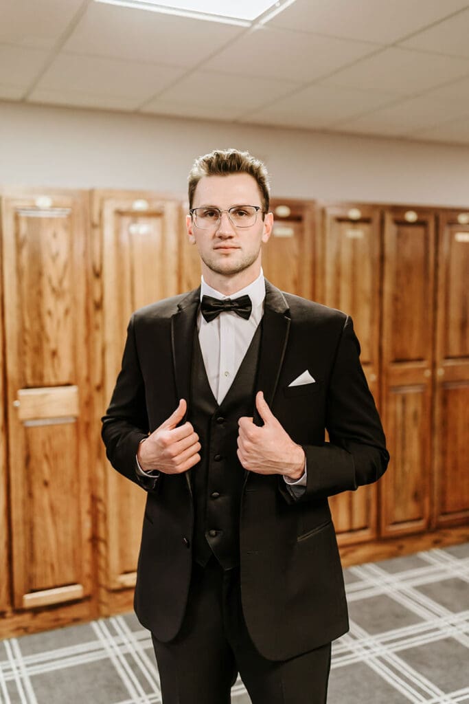 Groom adjusting his suit jacket while getting ready in the locker room at Running Deer Golf Club.