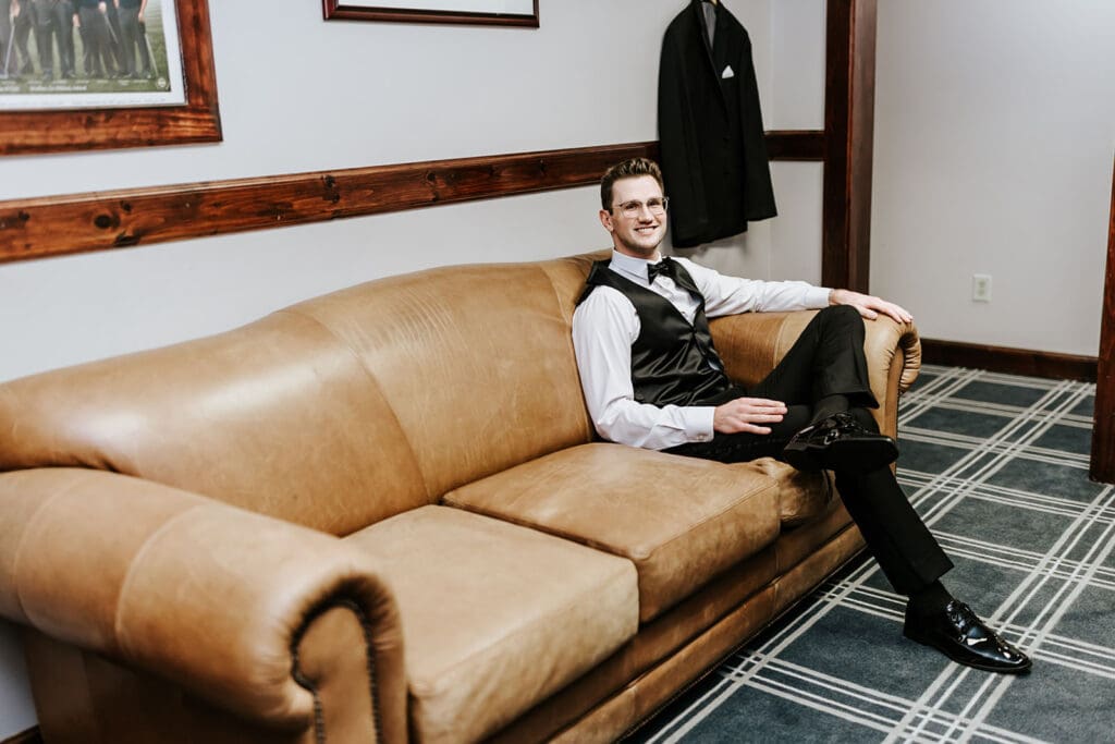 Groom relaxing on a leather couch in the men’s locker room before the ceremony at Running Deer Golf Club.