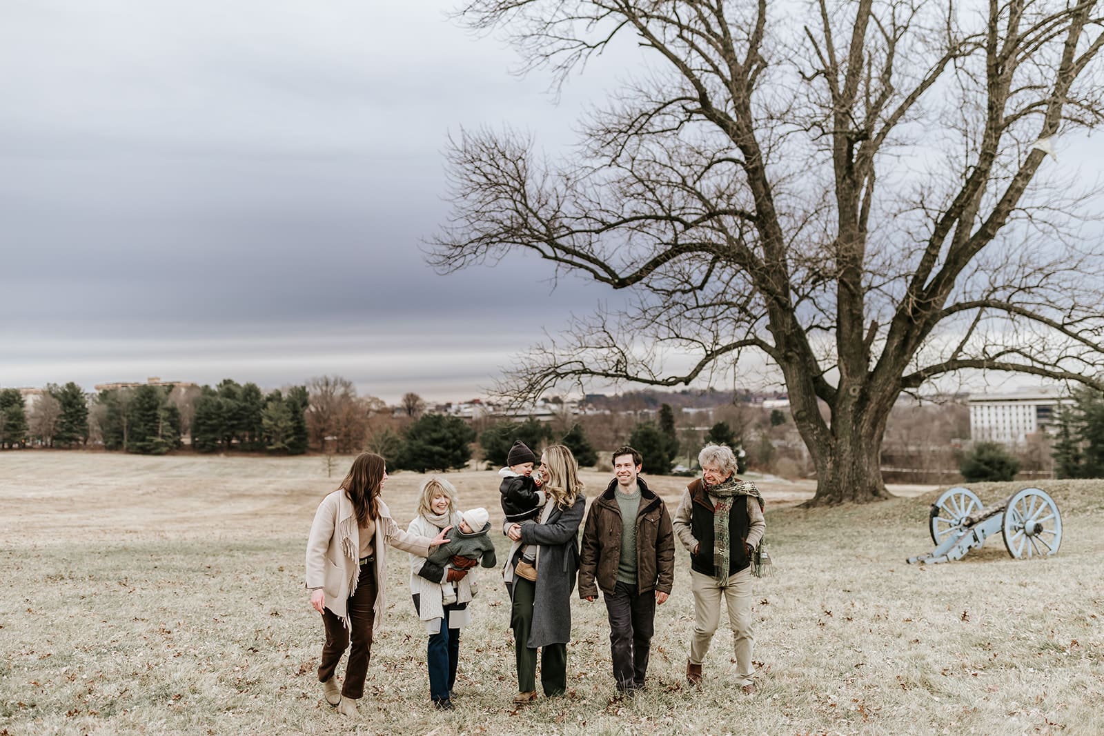 Extended family walking together during a winter family photography session at Valley Forge Historic National Park, with three generations bundled in neutral outfits near the historic cannons after Christmas.
