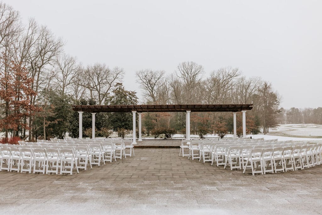 Outdoor wedding ceremony space at Running Deer Golf Club in Pittsgrove, New Jersey, featuring white chairs arranged beneath a pergola with winter landscape views.