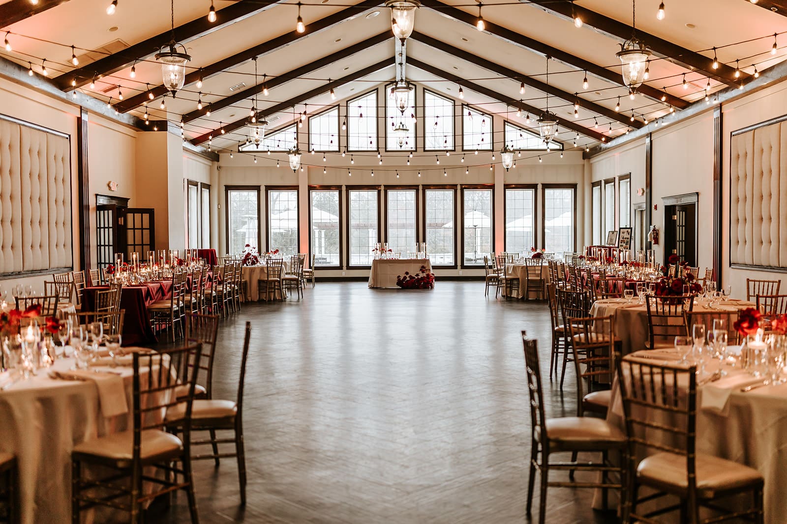 Elegant ballroom set up for a wedding showcase at Running Deer Golf Club in Pittsgrove, New Jersey, featuring round tables, café lighting, and a bright open reception space.