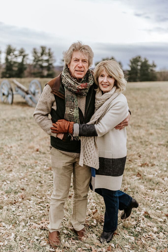 Grandparents hugging during an extended family photo session at Valley Forge Historic National Park, captured in winter with historic cannons and open fields in the background.