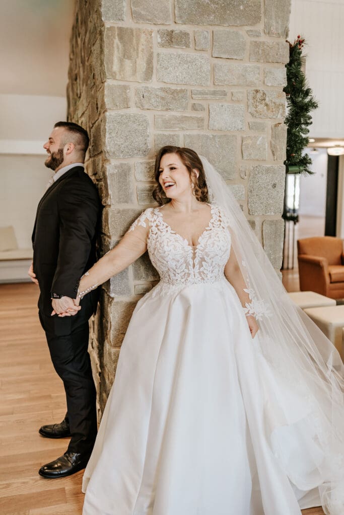 Bride and groom holding hands around a stone fireplace during a first touch inside Westwynd Gardens in Honey Brook, PA before their winter ceremony.