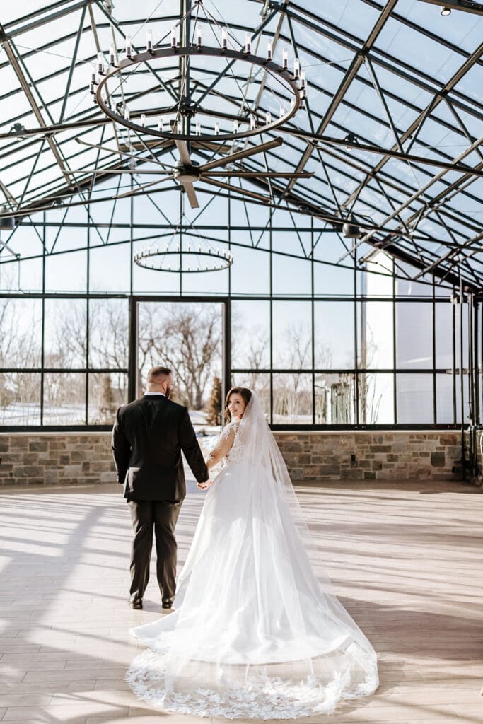 Bride and groom walking hand in hand inside the Westwynd Gardens greenhouse in Honey Brook, PA during their winter wedding ceremony.