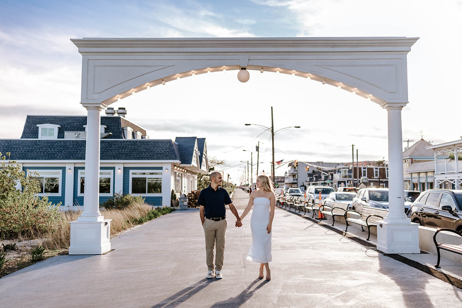 Couple walking hand in hand beneath the iconic archway near Congress Hall during their Cape May engagement session.