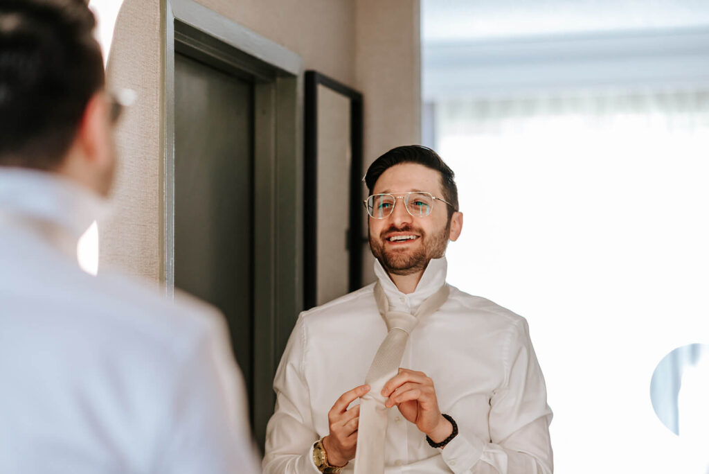 Groom getting ready and adjusting his tie before wedding at The Merion