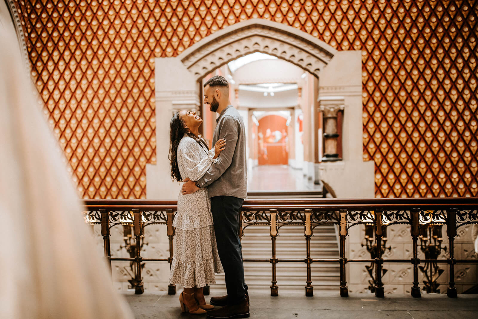 couple laughing together on an ornate balcony during their PAFA engagement photos in Philadelphia.